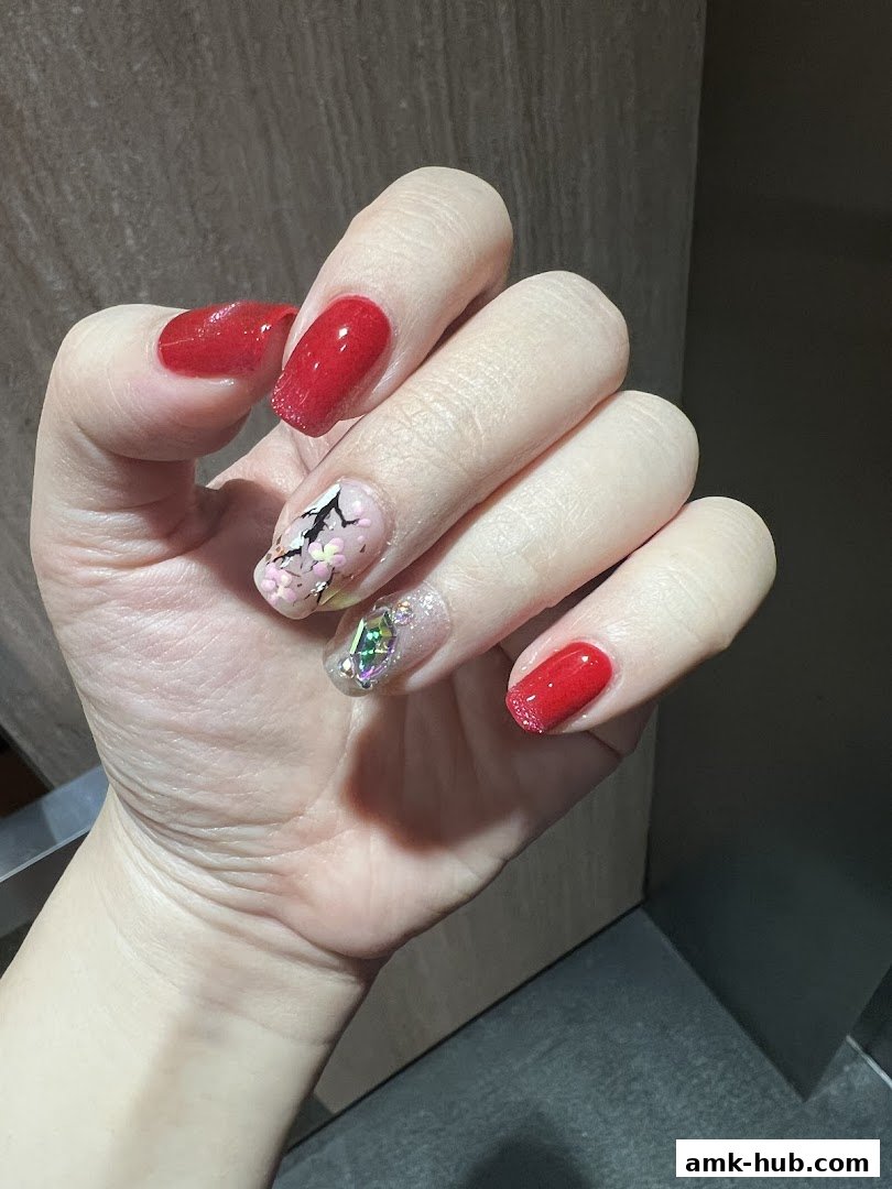 A hand with beautifully designed red nails, featuring intricate nail art and sparkling gems.
