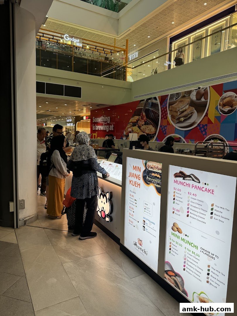 A brightly lit food stall in a mall selling pancakes and kueh with customers ordering.
