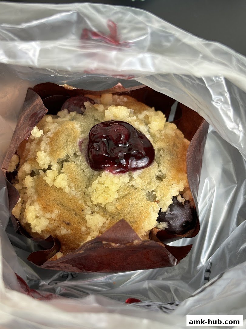 A close-up of a blueberry muffin with crumble topping, inside a plastic bag.
