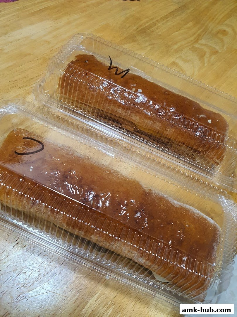 Two apple strudels in clear plastic containers on a wooden surface.