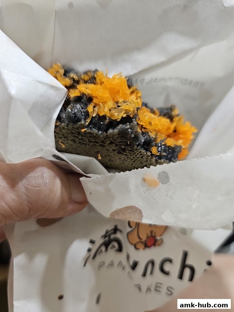 A close-up of a black sesame pancake topped with shredded orange candy.