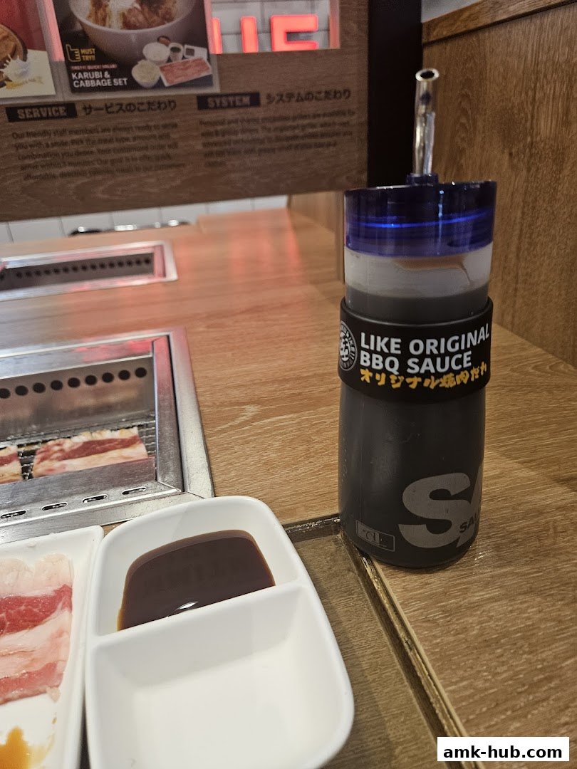 A bottle of BBQ sauce sits on a table next to raw meat and dipping sauce.