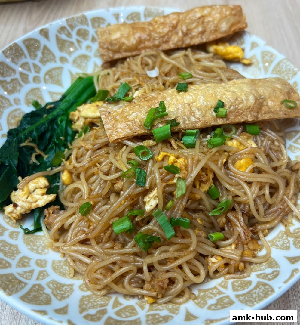 A close-up shot of a delicious noodle dish with fried tofu skin and greens.