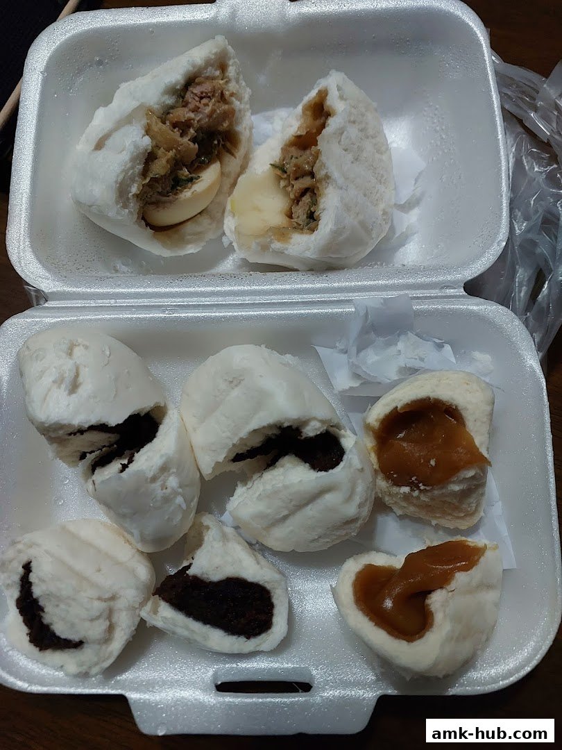 A white styrofoam container filled with various steamed buns, some with savory fillings and others with sweet fillings.