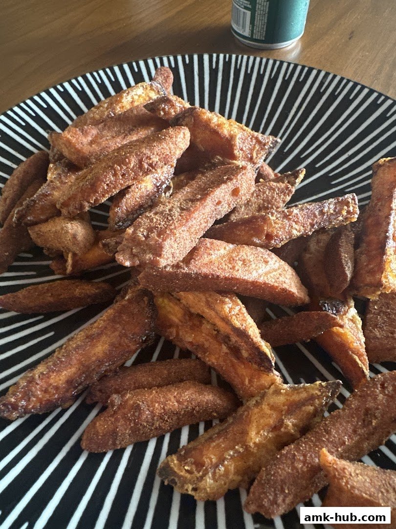 A plate of crispy, seasoned sweet potato fries served on a black and white striped plate.