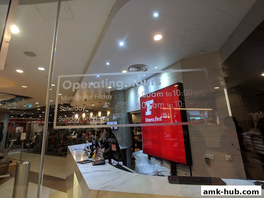 The entrance of Fitness First gym with operating hours displayed on the glass.