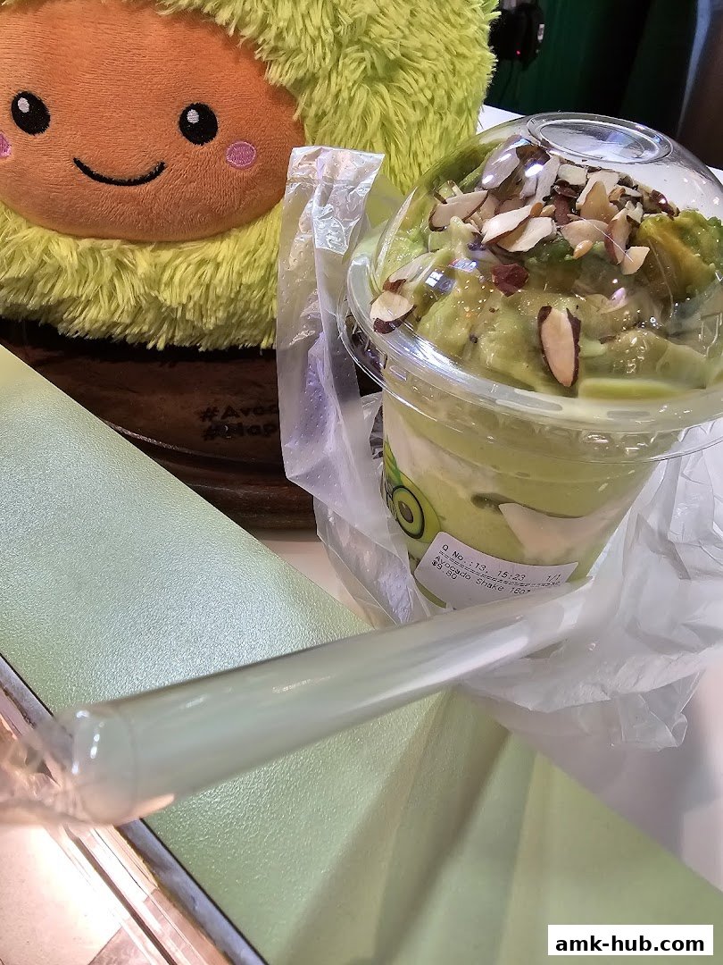 A close-up of an avocado shake with almonds and a plush avocado toy.
