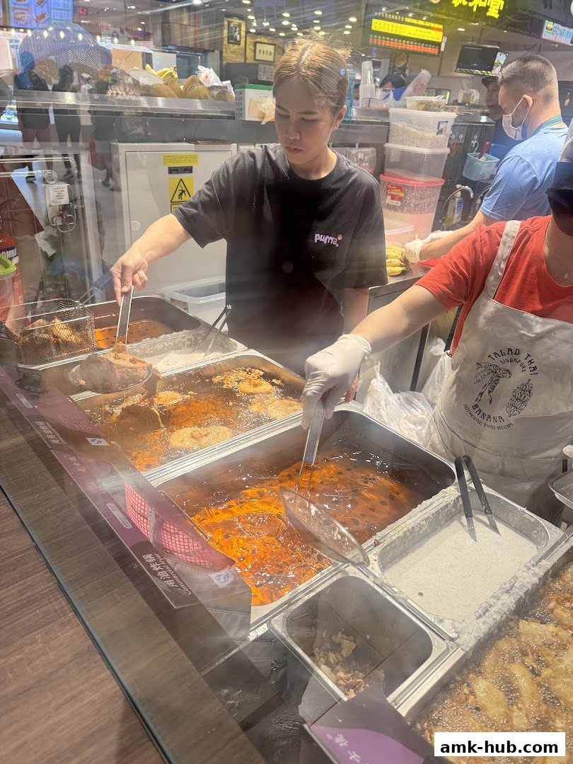Staff preparing fried food at a Thai banana stall, with bubbling oil and ingredients.