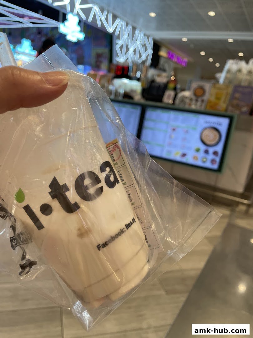 A hand holds a plastic-wrapped drink from iTEA with a blurred background of the shop.