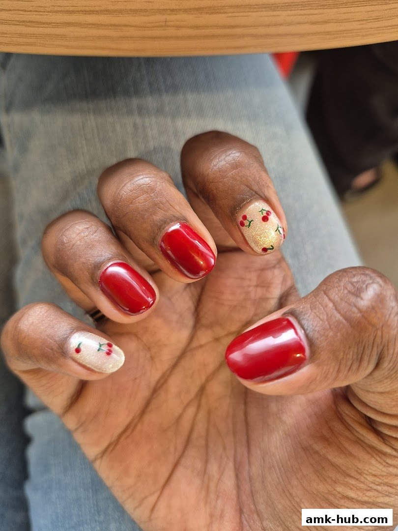 A close-up of a hand with glossy red nails and accent nails featuring a cherry design.
