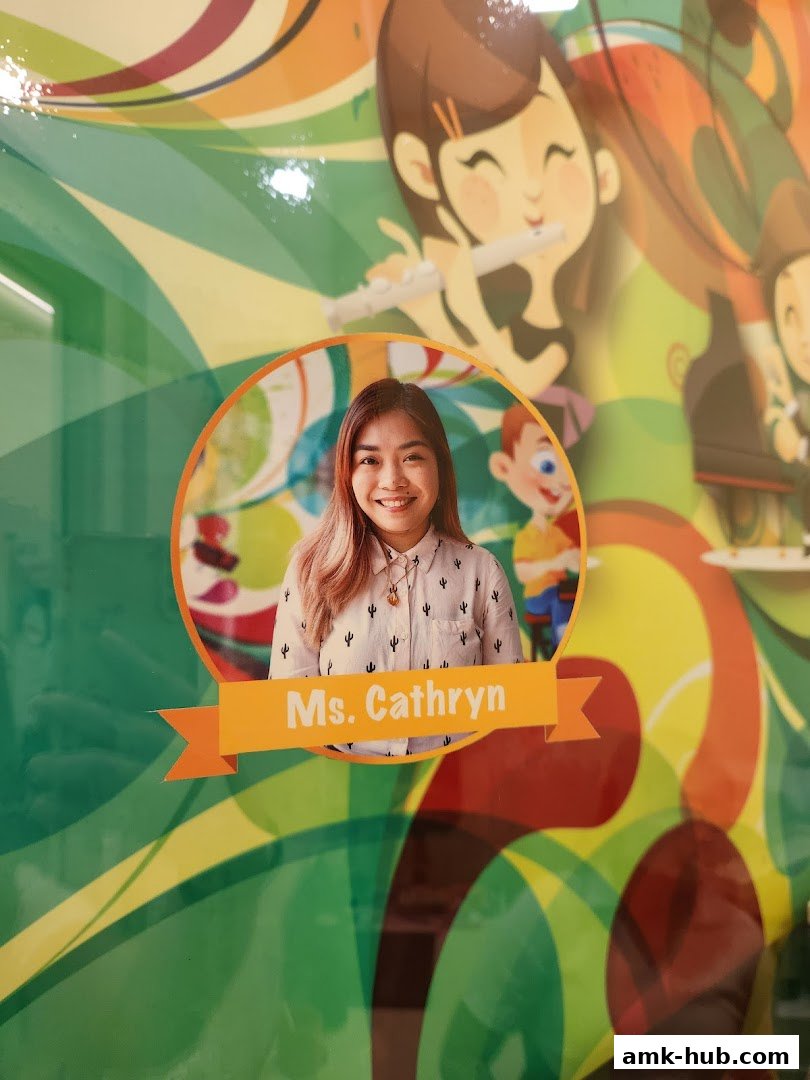 A portrait of Ms. Cathryn with a colorful, cartoonish background featuring children playing music.