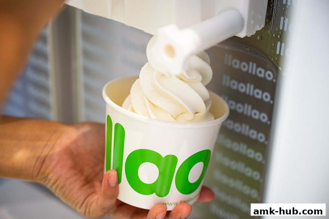 A hand holds a cup of frozen yogurt being dispensed from a machine.