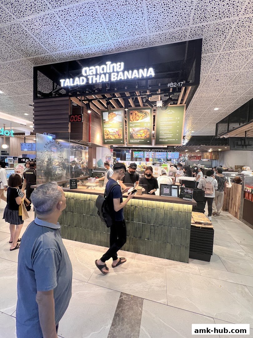 A busy food stall with customers ordering at the counter and a prominent sign for Talad Thai Banana.