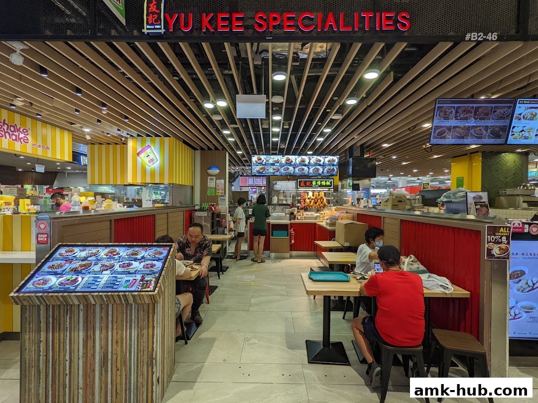 A food stall with a digital menu and seating area, displaying various dishes.