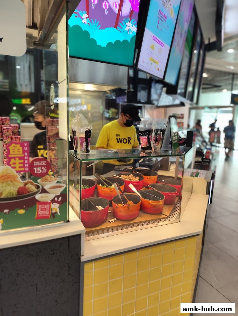A Wok Hey staff member in a yellow shirt serves food behind a counter with ingredients.