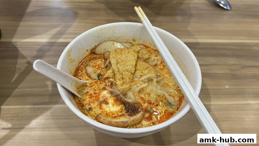 A close-up shot of a delicious bowl of Laksa with chopsticks and a spoon.