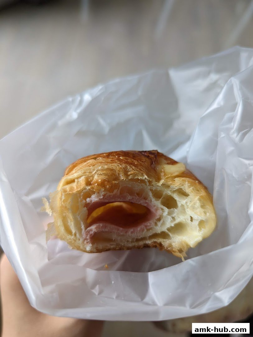 A close-up shot of a ham and cheese croissant in a white plastic bag.