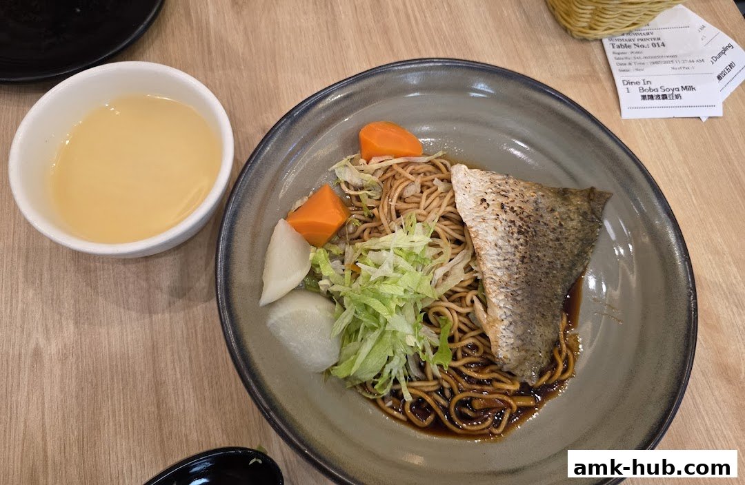 A bowl of noodles with fish, vegetables, and a side of soup, with a receipt visible.