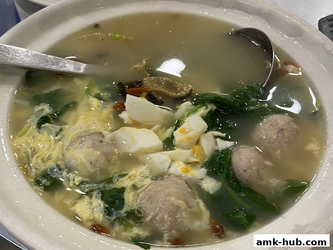 A close-up shot of a steaming bowl of soup with meatballs, vegetables, and egg.