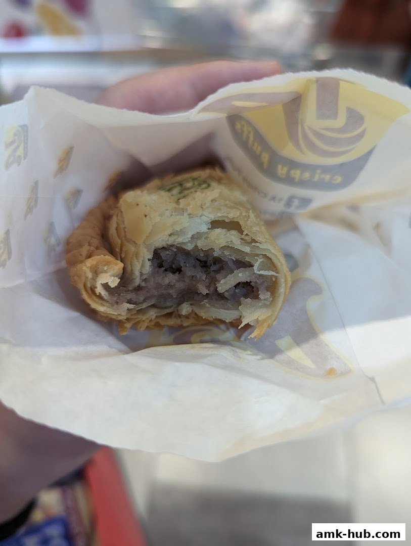 A person holds a partially eaten savory pastry in a branded paper bag.