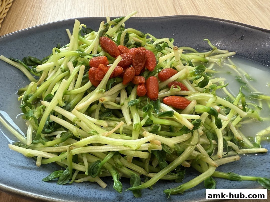 A close-up of a plate of stir-fried pea shoots with goji berries.