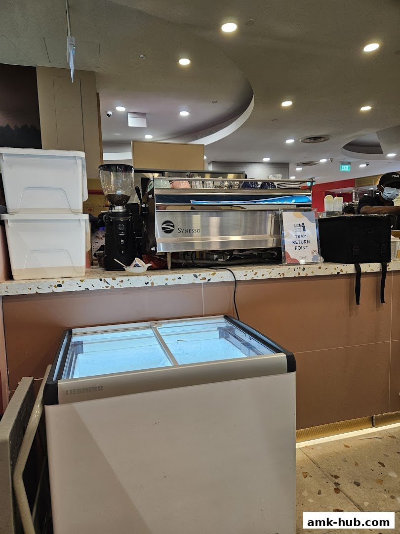 A coffee machine and grinder are displayed behind a counter with a freezer in the foreground.