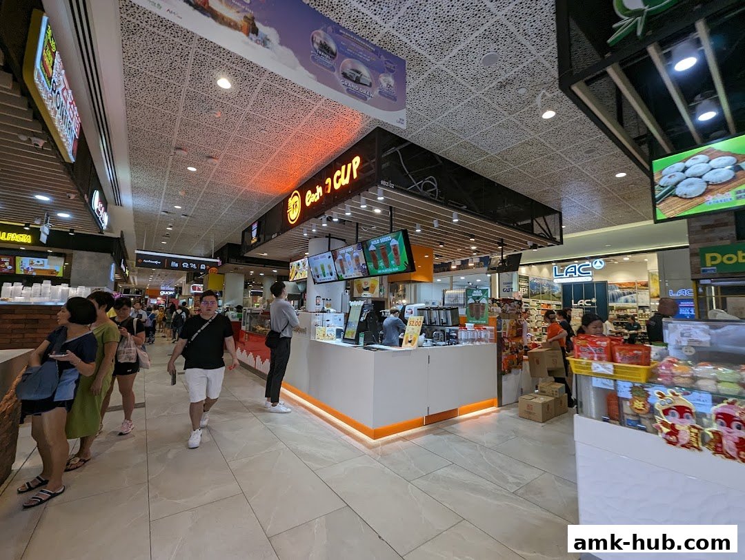 A busy shopping mall corridor with an 'Each A Cup' beverage shop and other stores.