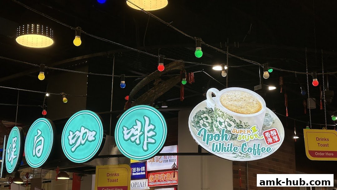 Signs for Ipoh White Coffee and other food items hang from the ceiling with decorative lights.