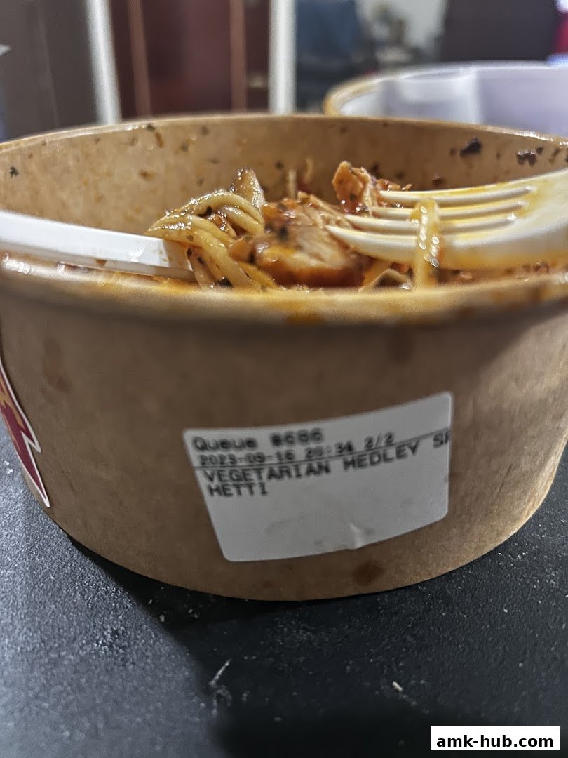 A close-up of a bowl of pasta with chicken and a fork, showing a label with order details.