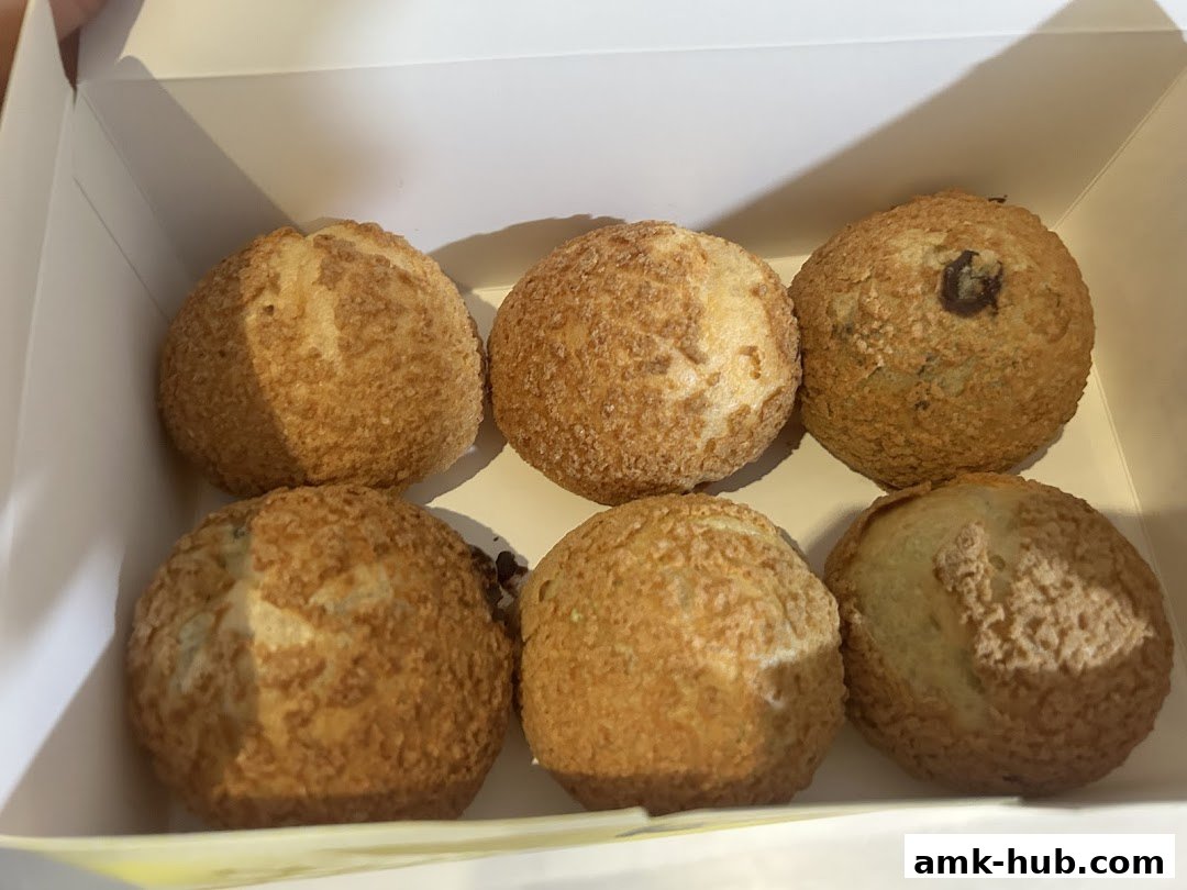A white box filled with six golden-brown cream puffs, some with chocolate chips.