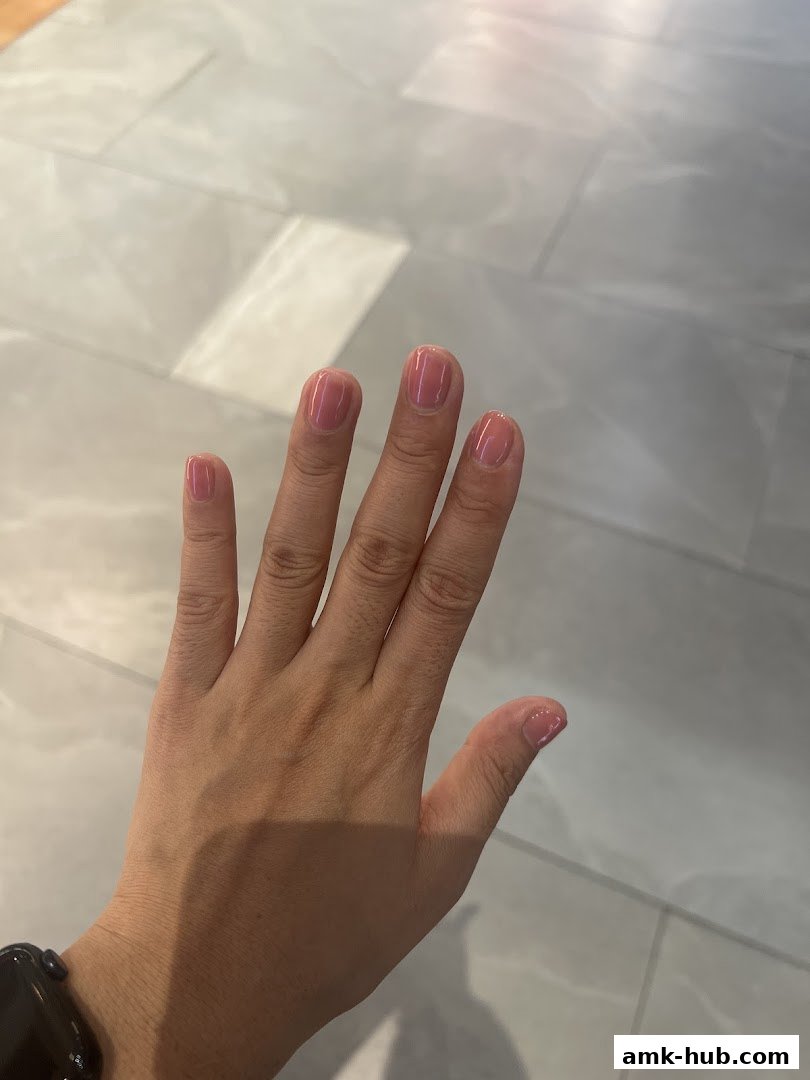 A hand with neatly manicured pink nails against a light-colored tiled background.