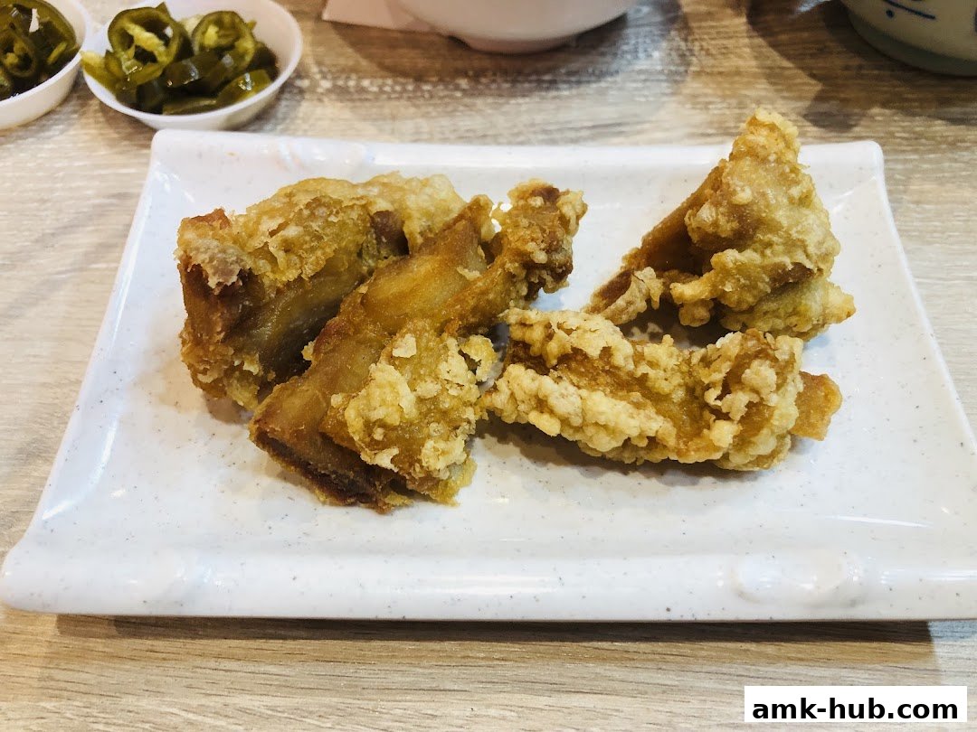 Crispy fried chicken pieces served on a white rectangular plate with pickled jalapeños in the background.