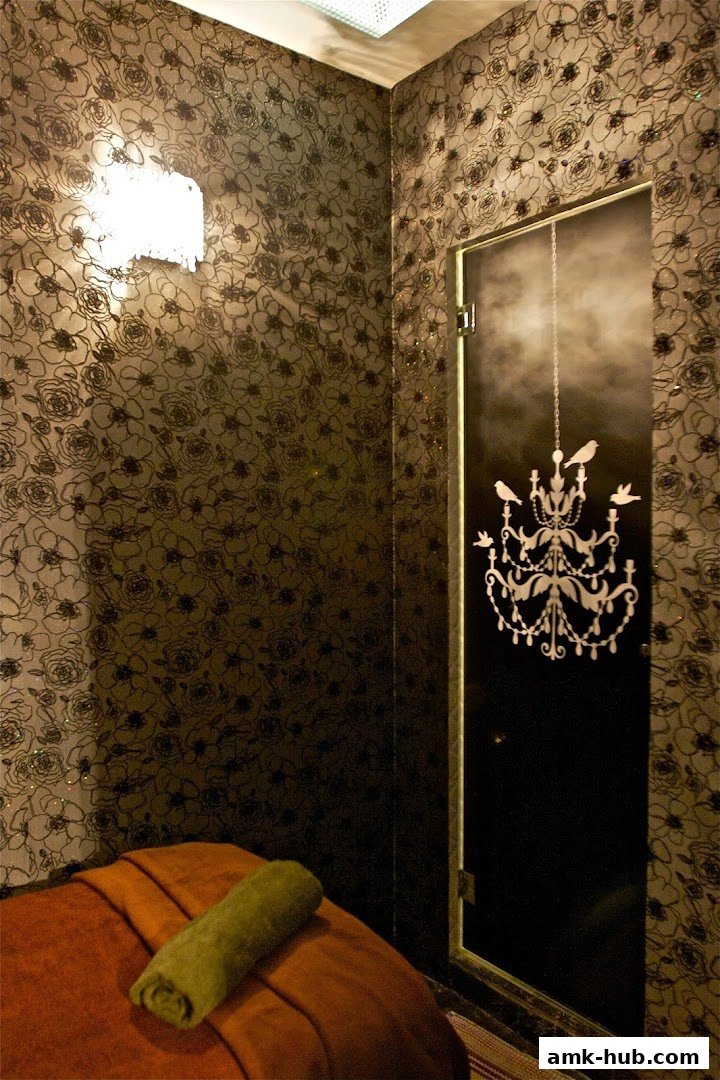 A dimly lit spa room with floral wallpaper, a massage bed, and a decorative door.