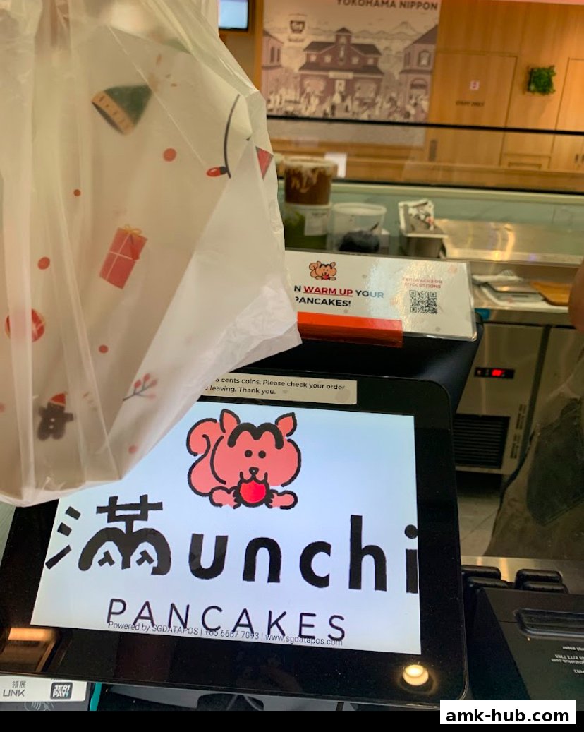 A close-up of a digital ordering screen for Munchi Pancakes with a branded bag in the foreground.