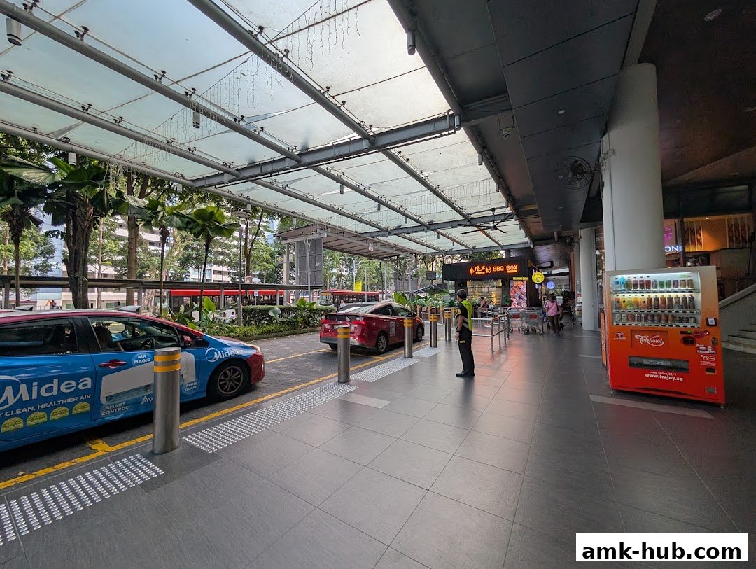 A taxi stand area with cars, a vending machine, and a covered walkway.