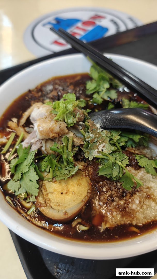 A close-up of a bowl of wanton noodles with braised egg and meat.