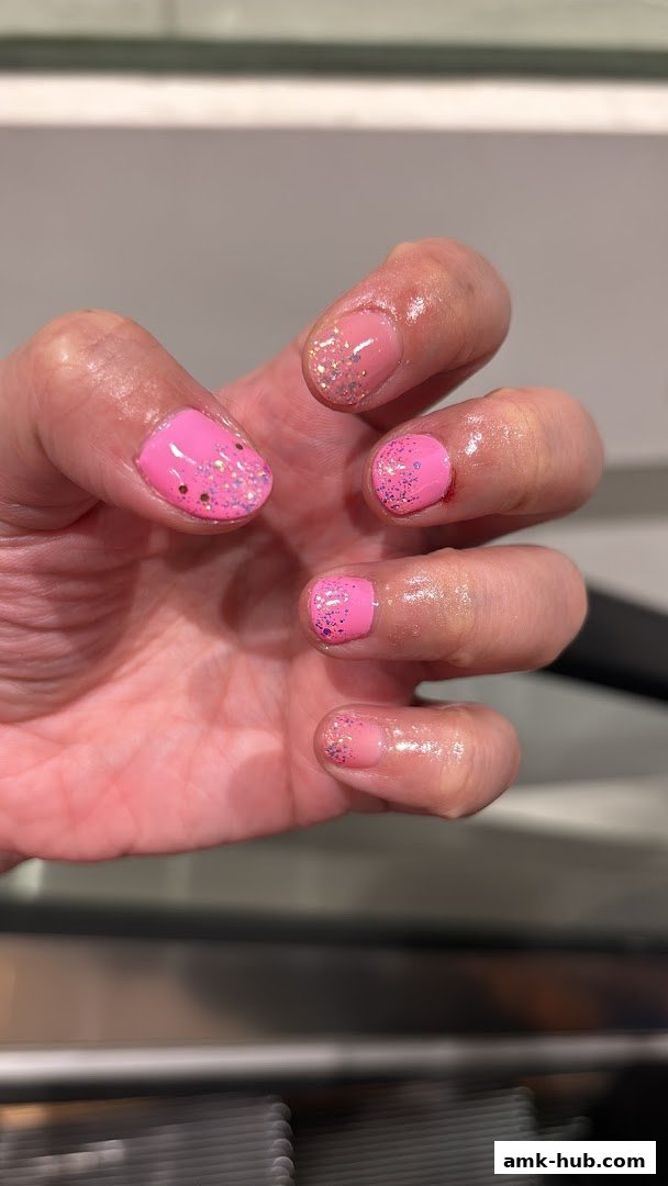 A close-up of a hand with bright pink nails adorned with glitter.