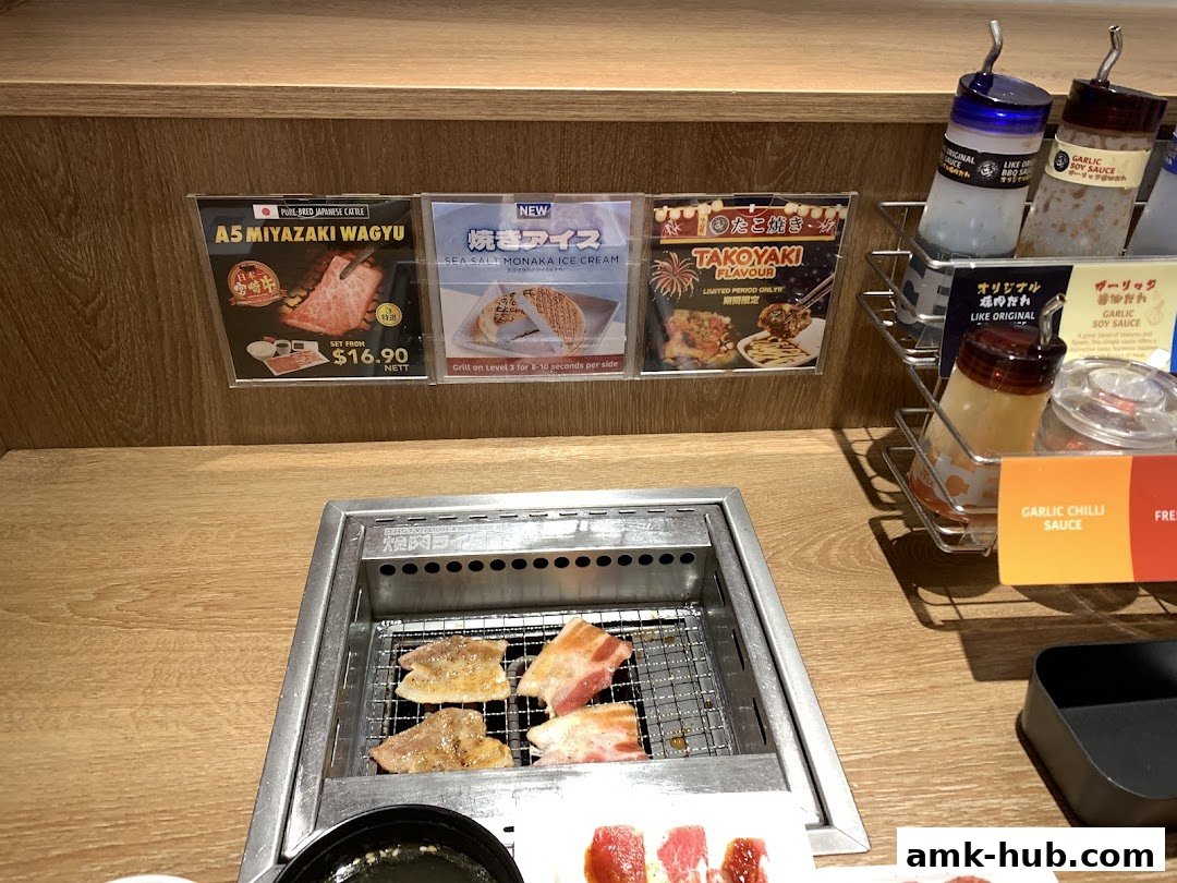 Grilling meat at a Yakiniku Like restaurant with various sauces and menu displays.
