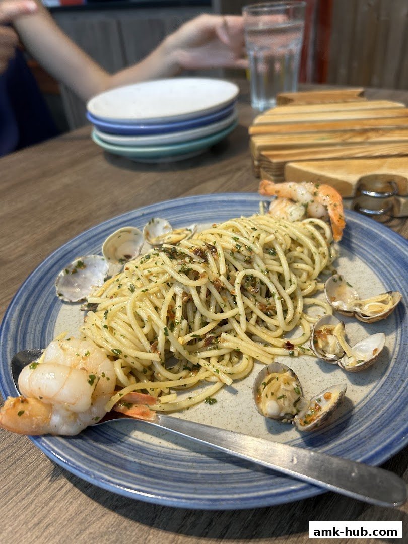 A plate of spaghetti with clams and shrimp, served with a glass of water and stacked plates.