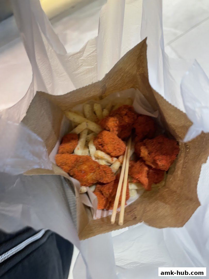 A paper bag filled with crispy fried chicken bites and french fries.