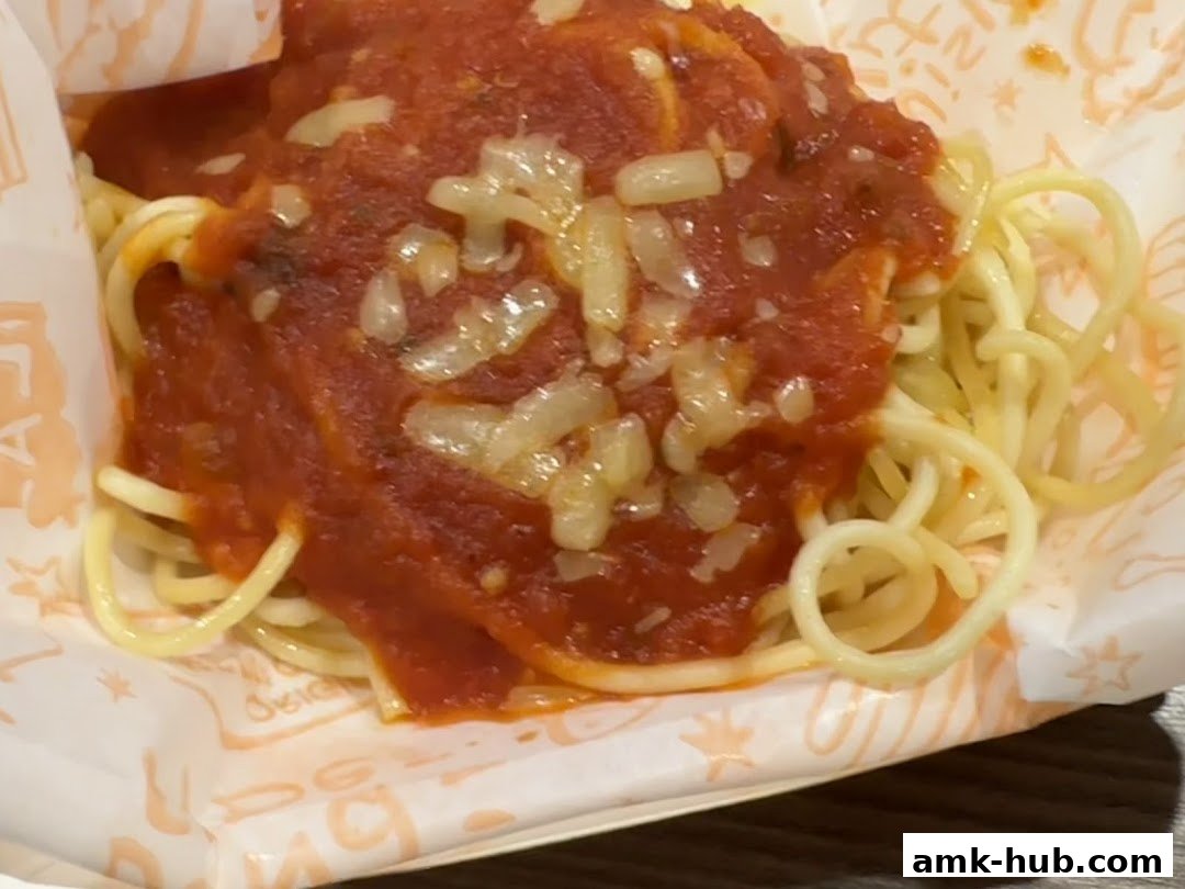 A close-up shot of spaghetti with marinara sauce and cheese, served in Popeyes branded paper.
