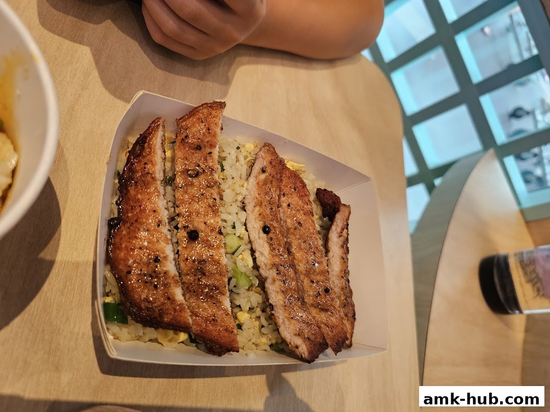 A close-up of a dish with sliced pork and fried rice, served in a paper container.