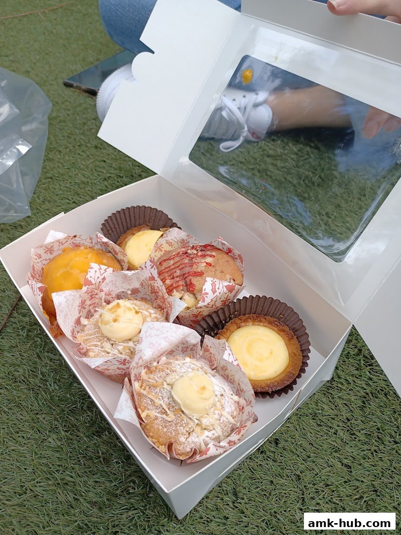 A white box filled with assorted pastries and muffins, presented on a grassy surface.