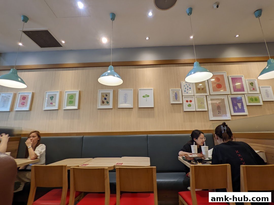 Interior of a MOS Burger restaurant with customers seated at tables and artwork on the wall.