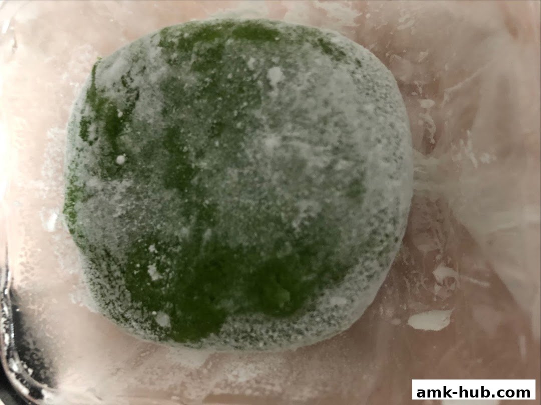 A close-up of a green mochi dusted with white powder, likely a dessert.