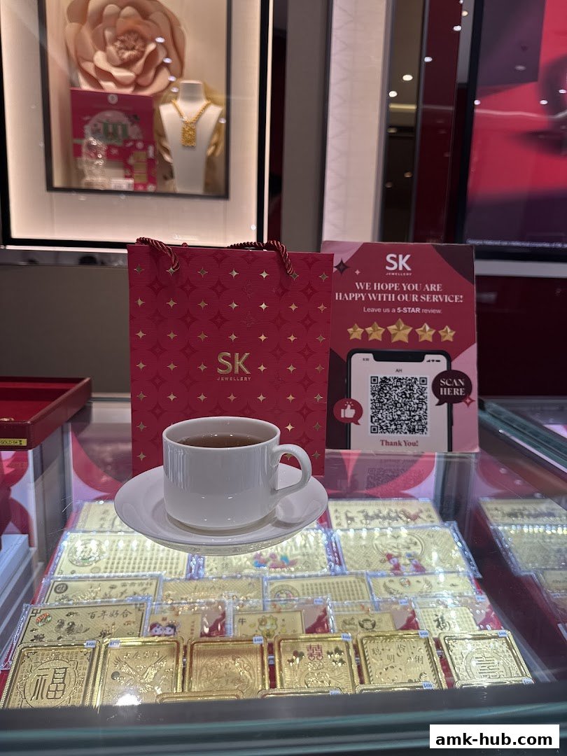 A display of gold bars and jewelry at SK Jewellery, with a cup of tea and a shopping bag.