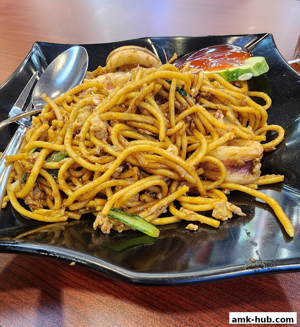 A plate of stir-fried noodles with squid and vegetables, served with a spoon and fork.