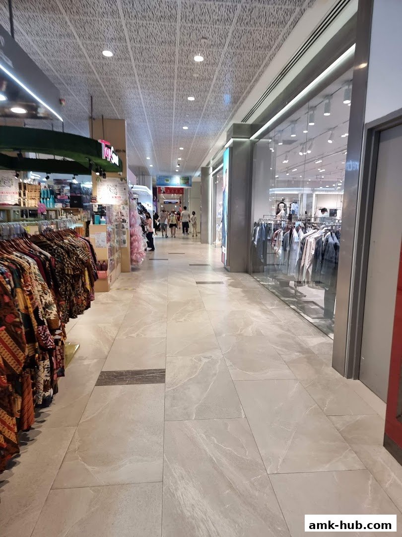 A view down a well-lit shopping mall corridor with clothing stores on either side.