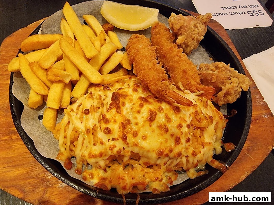 A sizzling platter of cheesy rice with fried shrimp, chicken, and french fries, garnished with a lemon wedge.