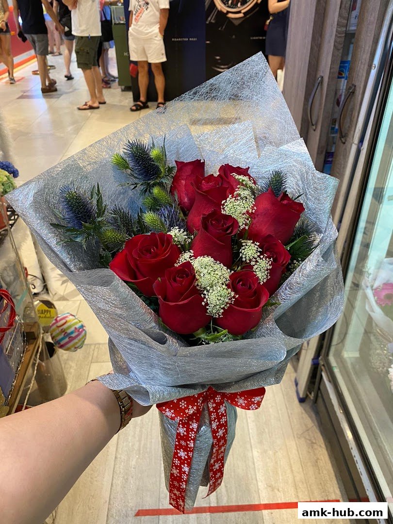 A hand holding a bouquet of red roses and thistles, wrapped in silver paper and tied with a festive ribbon.